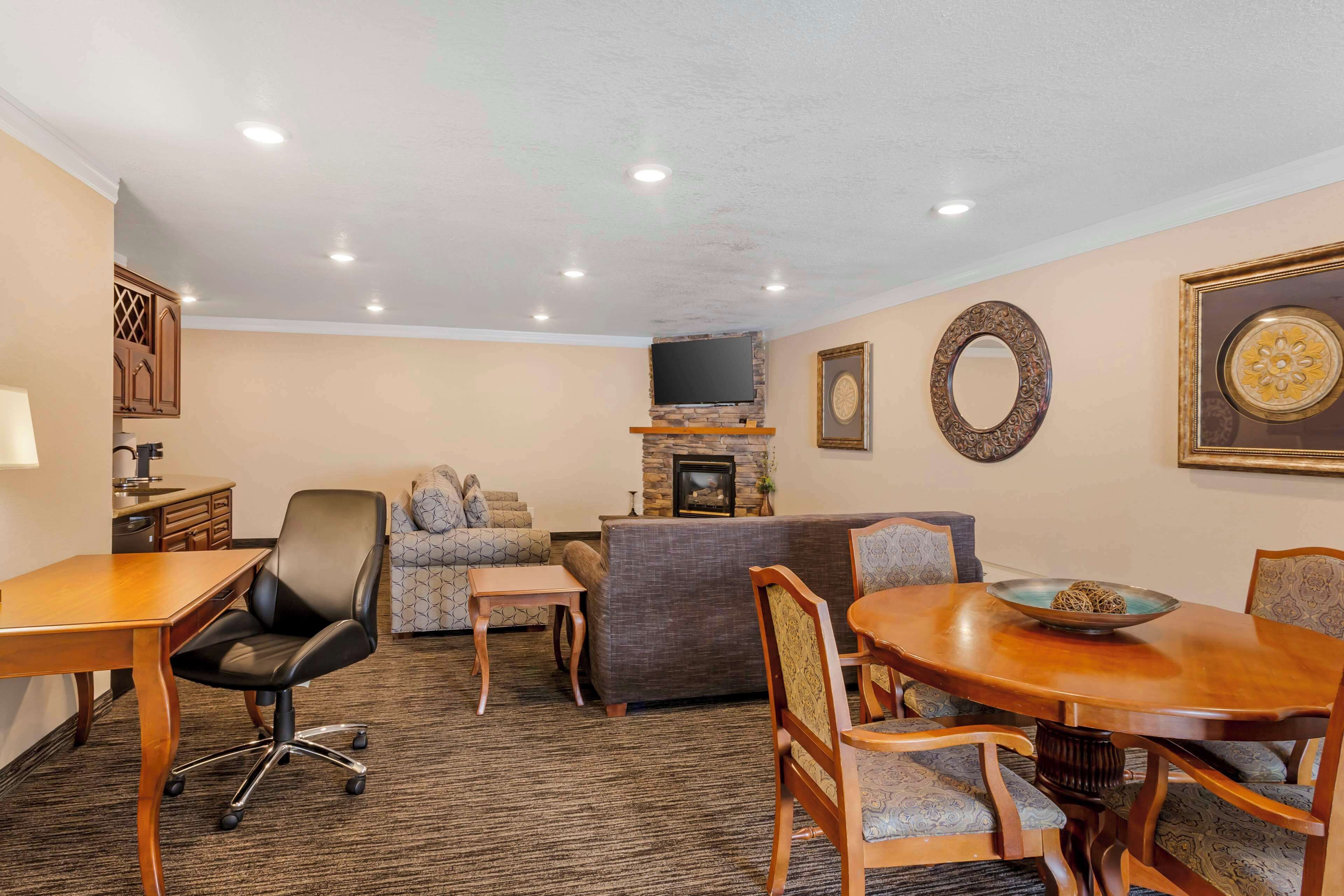 A hotel room with a dining area, a sofa, a fireplace, and a television.