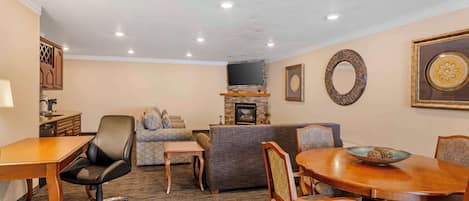 A hotel room with a dining area, a sofa, a fireplace, and a television.