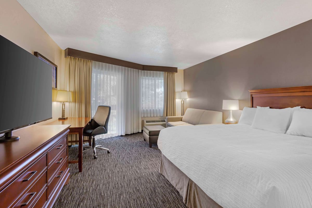 A hotel room with a large bed, a desk with a chair, a television, and two lamps.