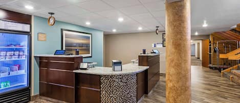 A reception area with a counter, a digital screen, and a refrigerator.