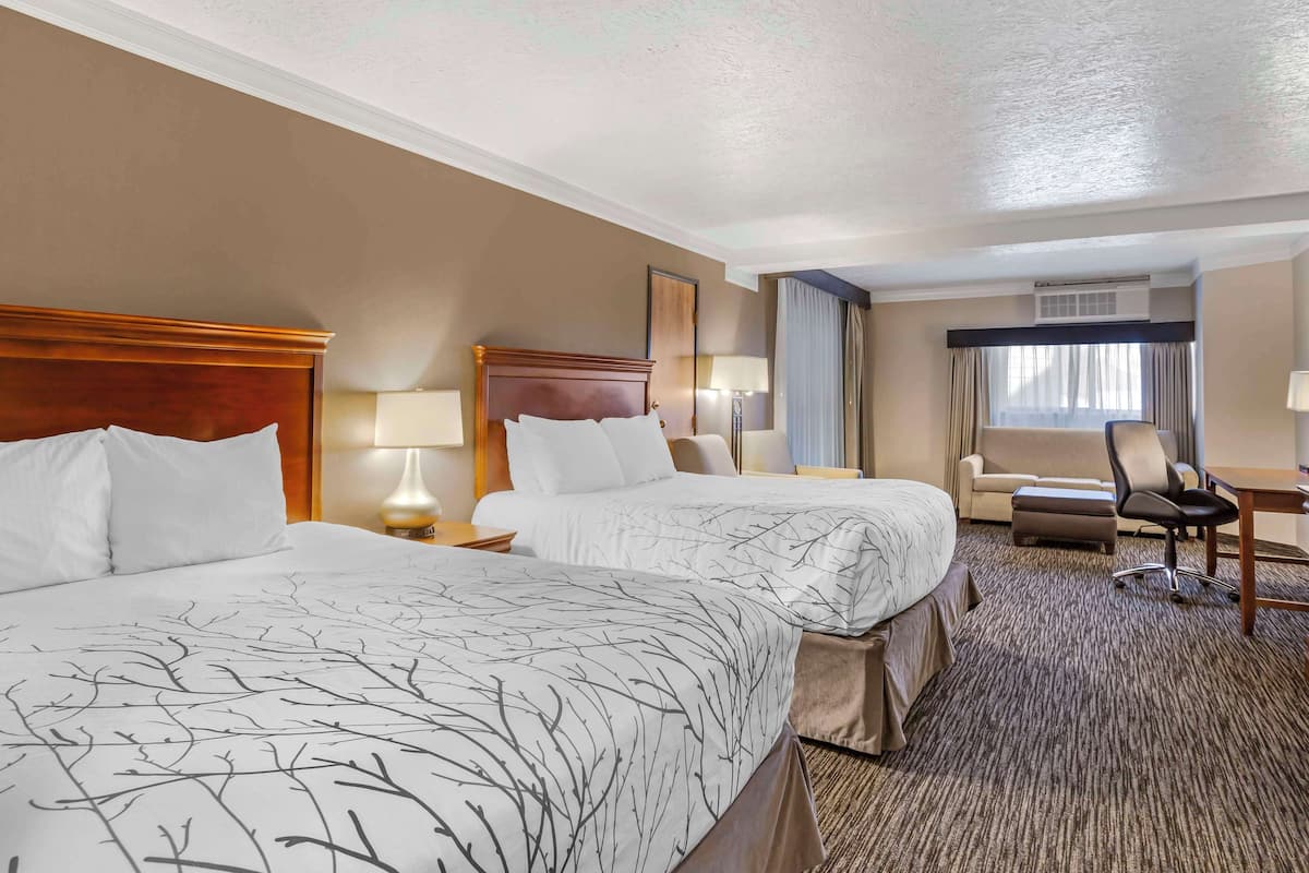 A hotel room with two beds, a desk, a chair, and a window with curtains.