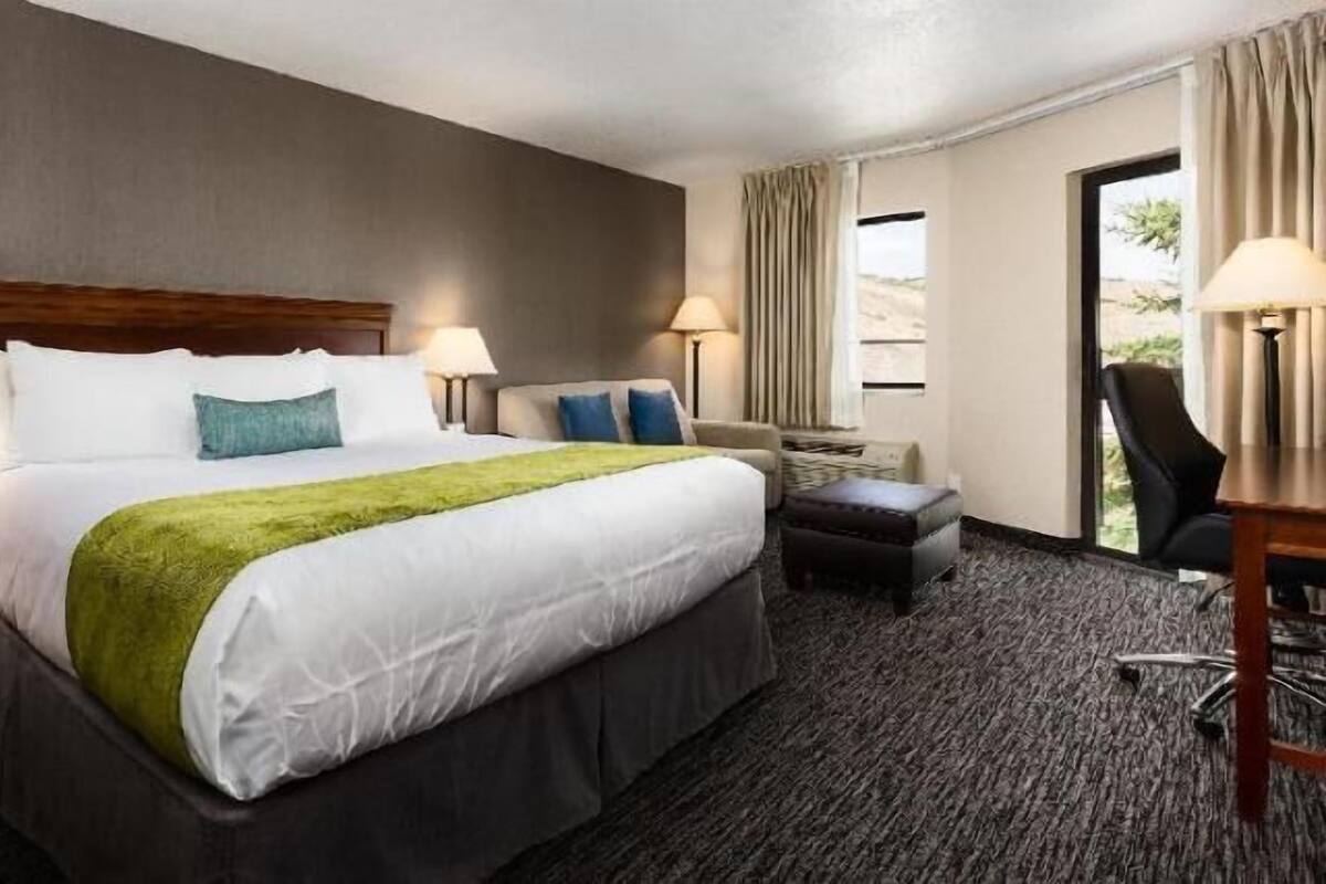 A hotel room with a large bed, two bedside tables with lamps, a chair, and a view of the outdoors.