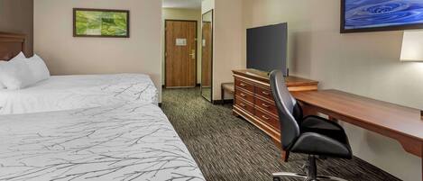 A hotel room with two beds, a desk, a chair, a TV, and artwork on the walls.