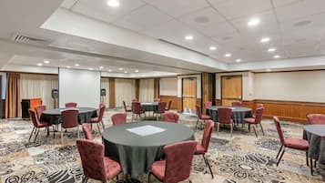 Une salle de conférence avec des tables rondes, des chaises rembourrées de couleur rouge et un sol recouvert de moquette.