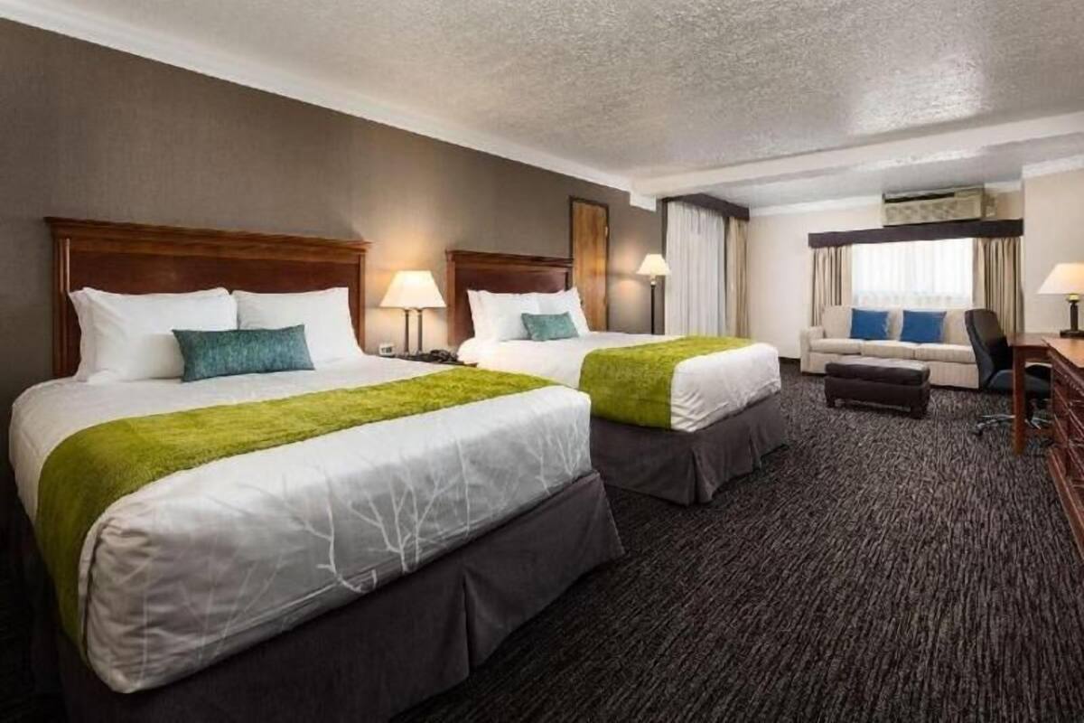 A hotel room with two beds, a desk, a chair, and a window with curtains.