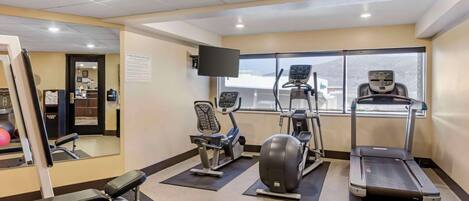 A gym with cardio machines, a mirror, and a window with a view.