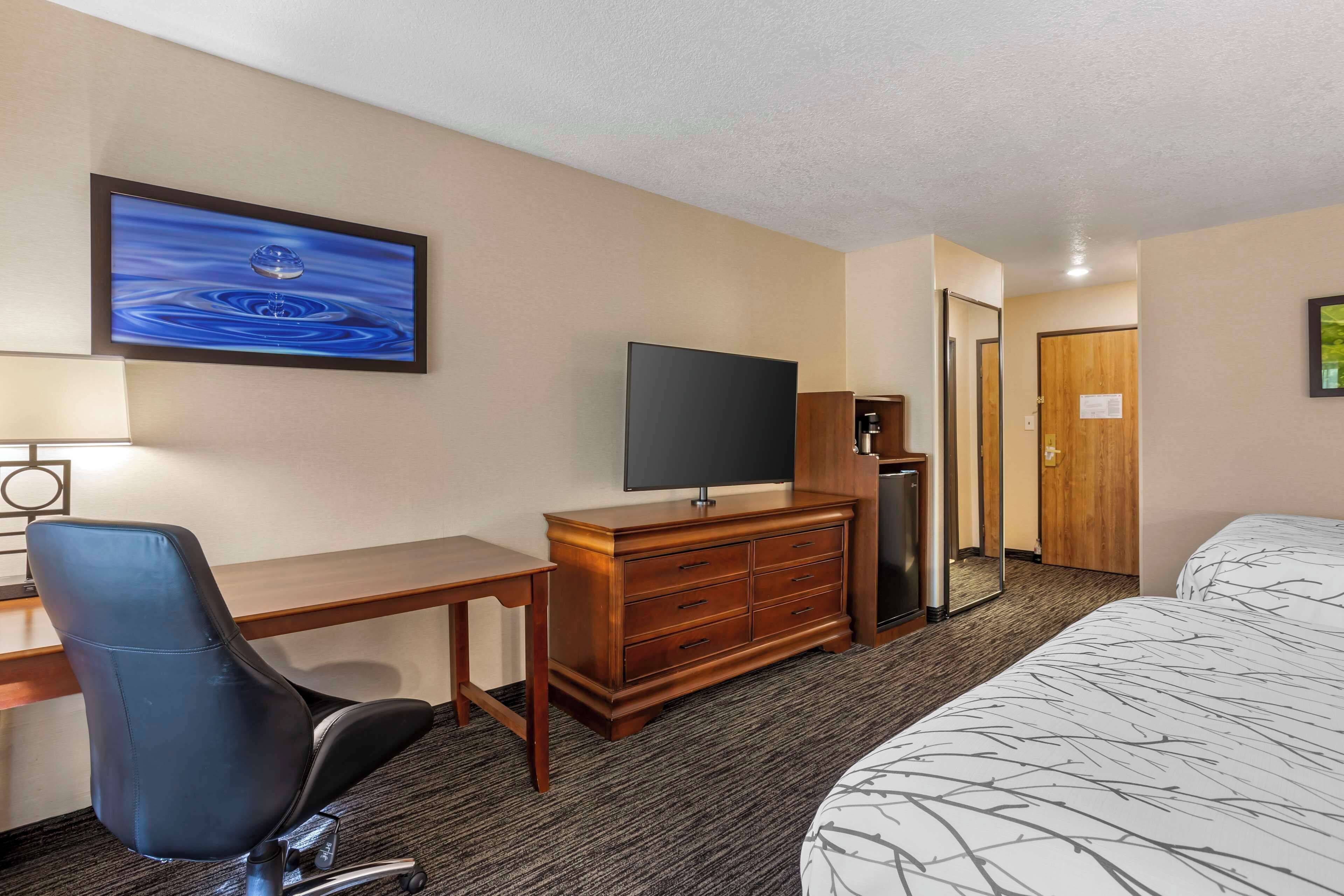 Une chambre d’hôtel avec un lit, un bureau, une chaise, une télévision, une commode et une porte.