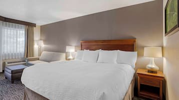 Ein Hotelzimmer mit einem großen Bett, zwei Nachttischen mit Lampen, einem kleinen Sofa und einem Fenster mit Vorhängen.