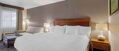 Una habitación de hotel con una cama grande, dos mesitas de noche con lámparas, un pequeño sofá y una ventana con cortinas.