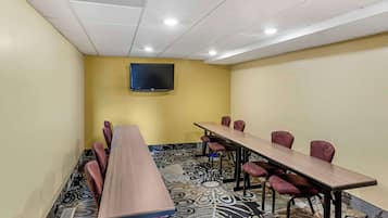 A conference room with a long table, chairs, a flat-screen TV, patterned carpet, and a yellow accent wall.