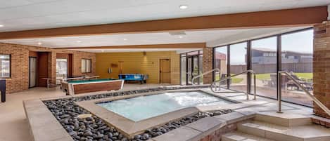 A pool area with a hot tub, a pool table, and a staircase leading to an outdoor patio.
