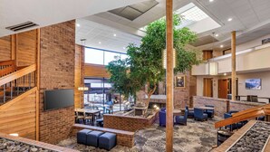 A spacious indoor area with a brick wall, a wooden staircase, a large tree, and seating areas. - Best Western Plus Landmark Inn (Park City)