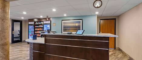 A reception area with a wooden counter, a refrigerator stocked with beverages, and a framed picture on the wall.