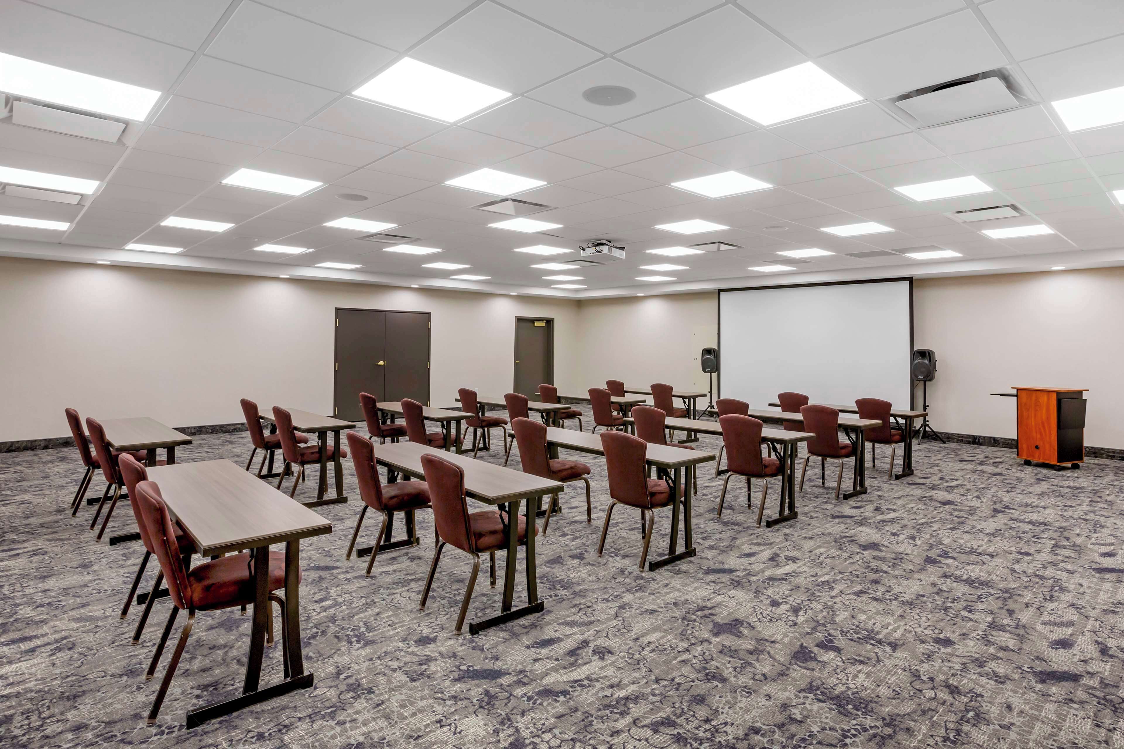 A conference room with tables and chairs, a projector, a screen, and a podium.