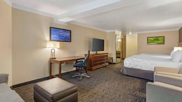 A hotel room with a bed, a desk with a chair, a TV, and a small seating area.