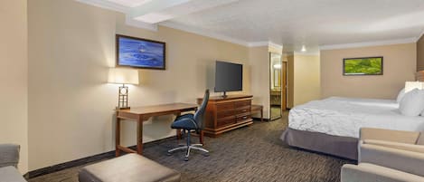 A hotel room with a bed, a desk with a chair, a TV, and a small seating area.