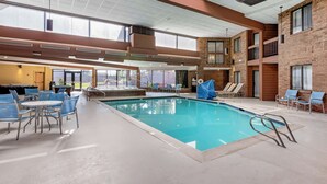 An indoor swimming pool with blue chairs and tables, large windows, and a brick wall. - Best Western Plus Landmark Inn (Park City)