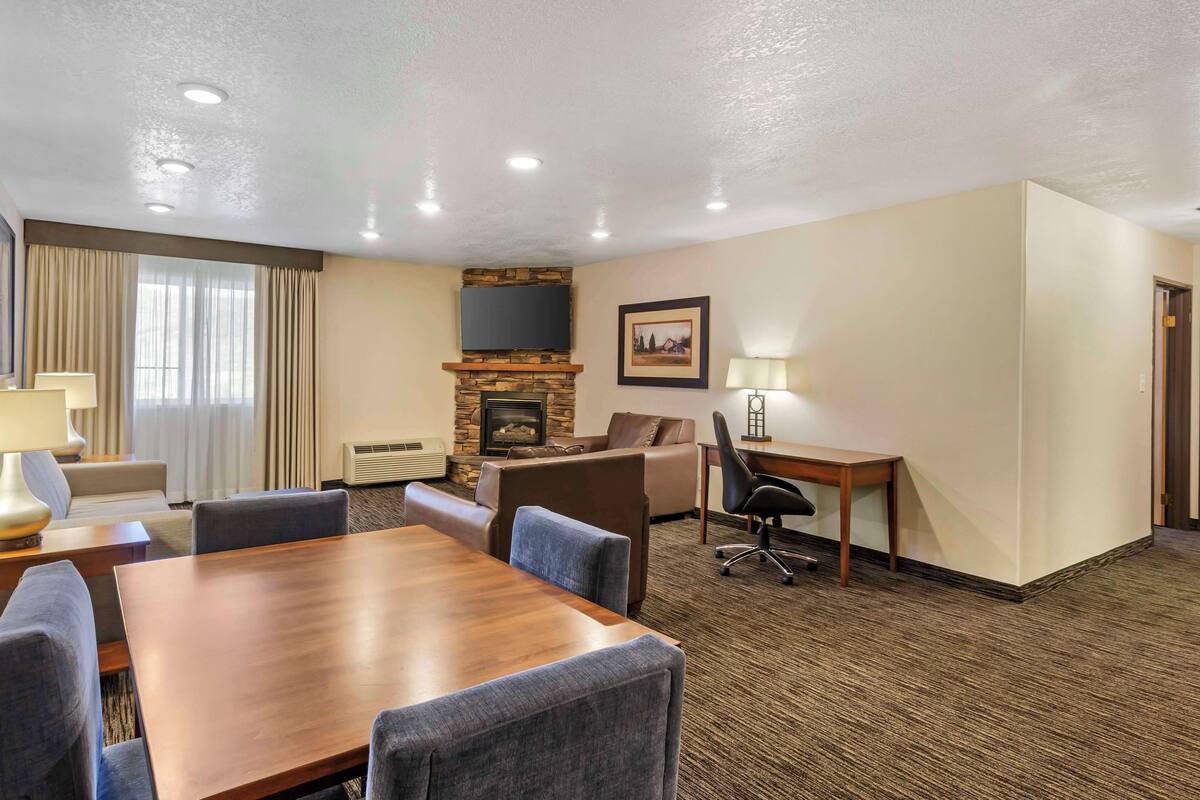A hotel room with a wooden dining table, comfortable seating, a fireplace, a flat-screen TV, and a framed picture on the wall.