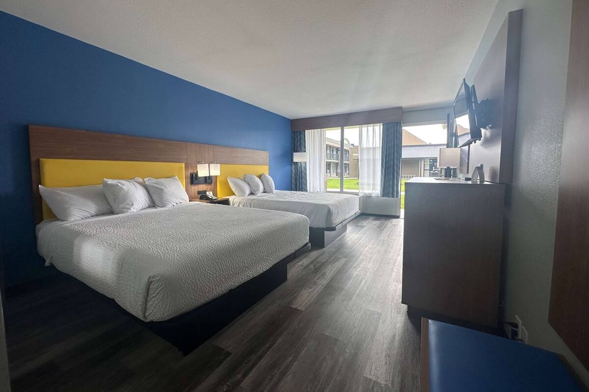 A hotel room with two beds, a TV, and a large window with a view of the outside.