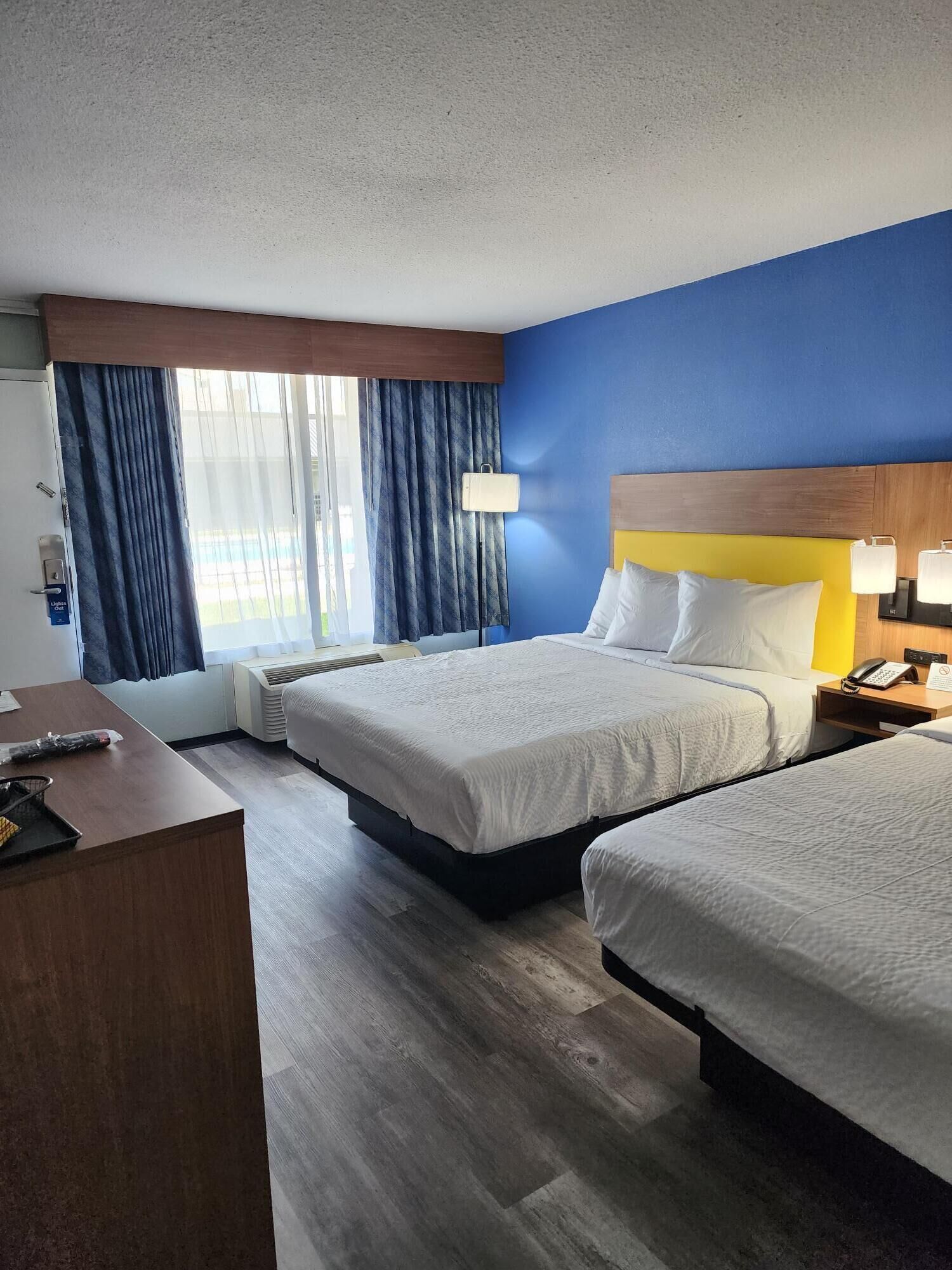 Habitación de hotel con dos camas, un escritorio, un teléfono y una ventana con cortinas.