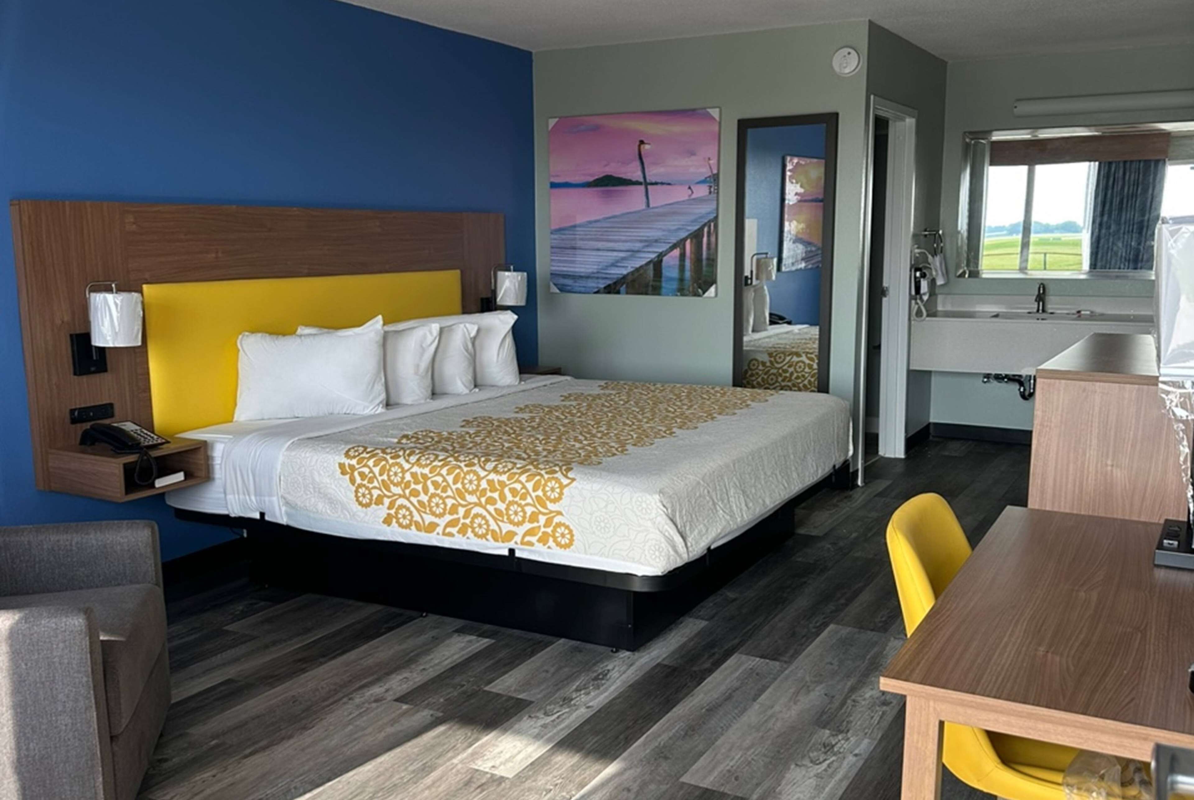 A hotel room with a large bed, a desk, a chair, a bathroom, and a painting on the wall.