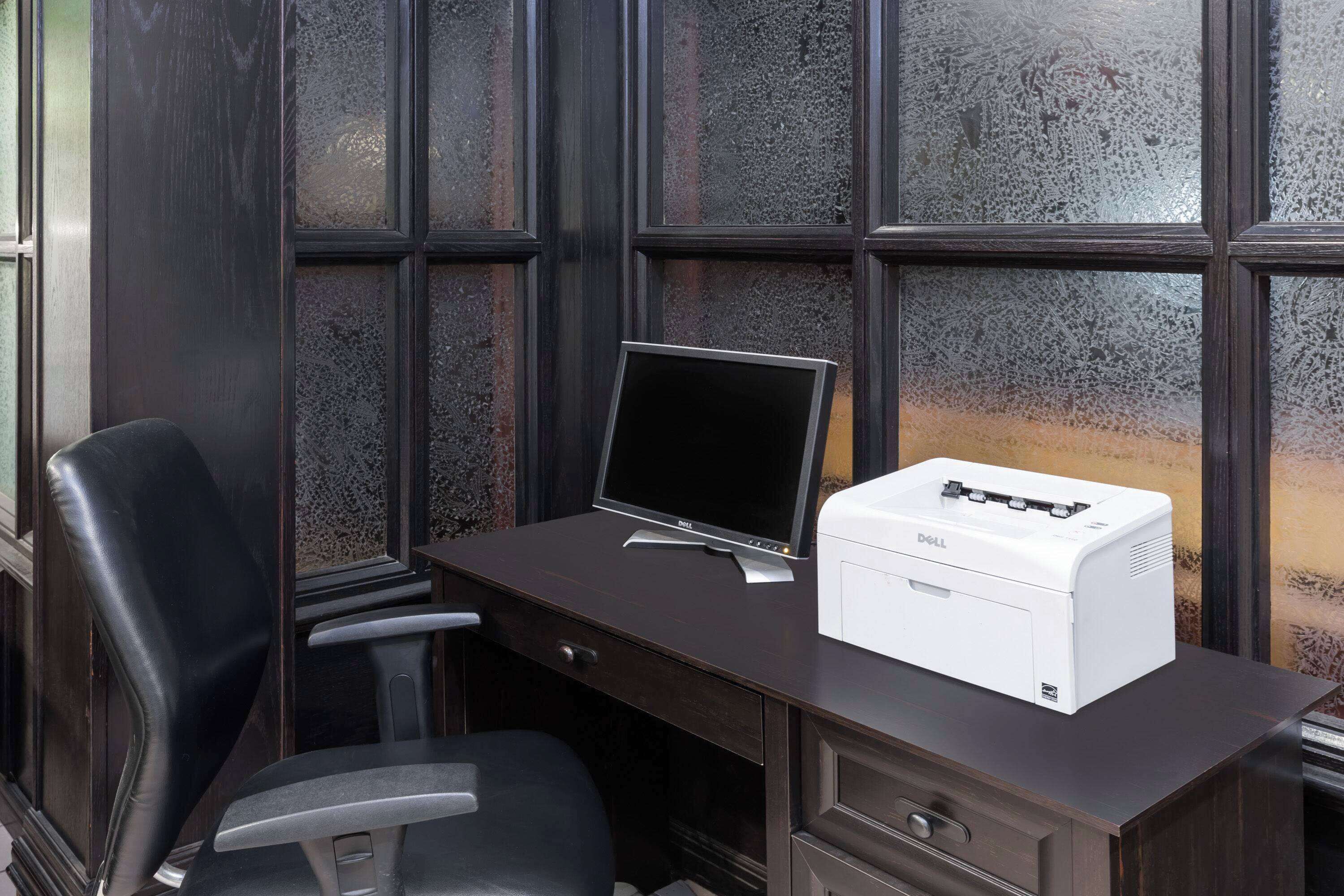 Un bureau en bois foncé, sur lequel se trouvent un écran d’ordinateur Dell et une imprimante.