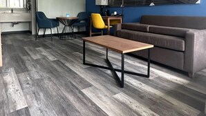 A modern living room with a wooden floor, a grey sofa, a yellow chair, and a blue wall with a sunset painting. - Days Inn & Suites by Wyndham Jennings (Jennings)