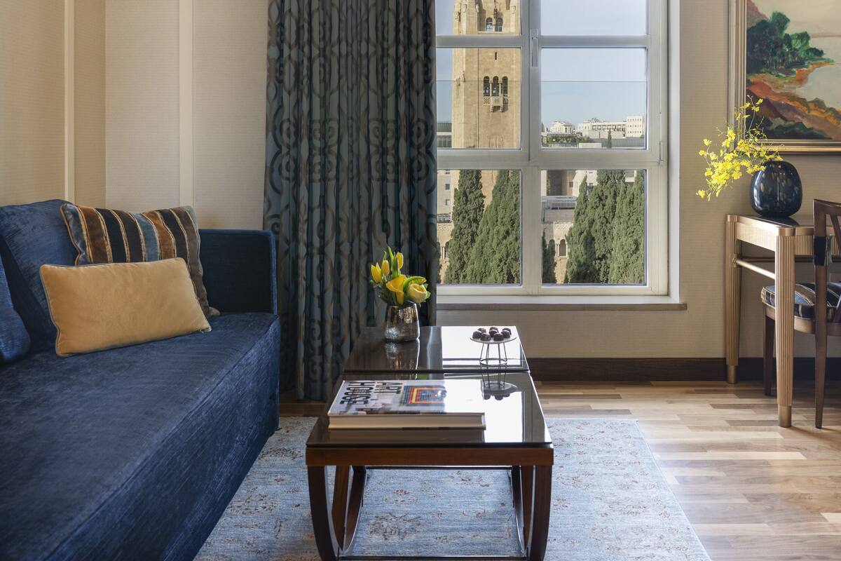 A living room with a large window, a sofa, a coffee table, and a painting on the wall.