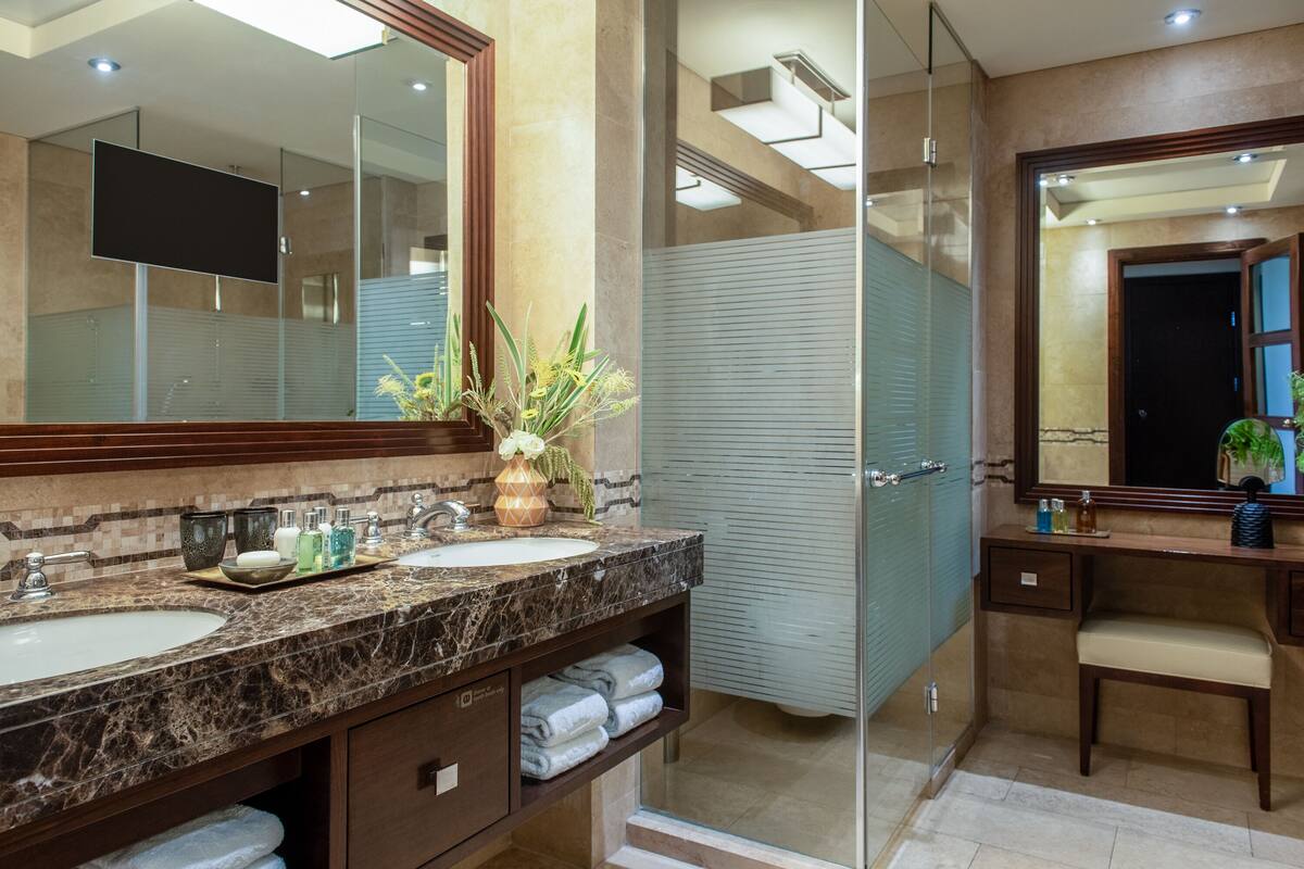 A modern bathroom with two sinks, a large mirror, and a shower area.