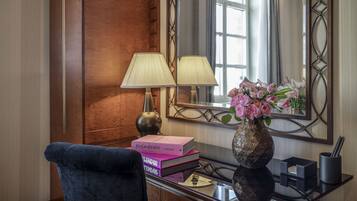 Una habitación de hotel con un panel de pared de madera, un espejo grande, un escritorio con una lámpara, un jarrón con flores y una silla.