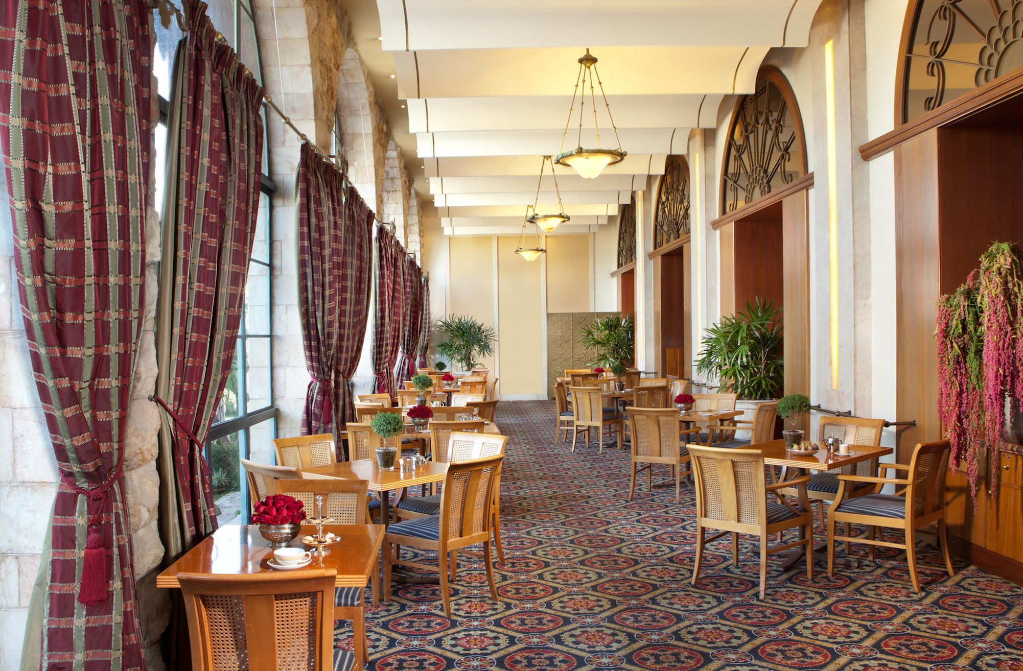 Vestíbulo de hotel con mobiliario de madera, alfombra estampada y ventanas grandes con cortinas.
