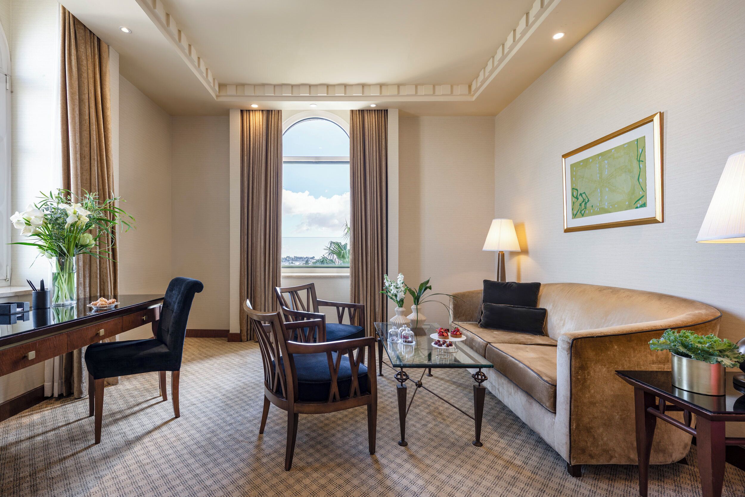 Een hotelkamer met een zithoek, een bank, een salontafel en uitzicht op het omliggende landschap.