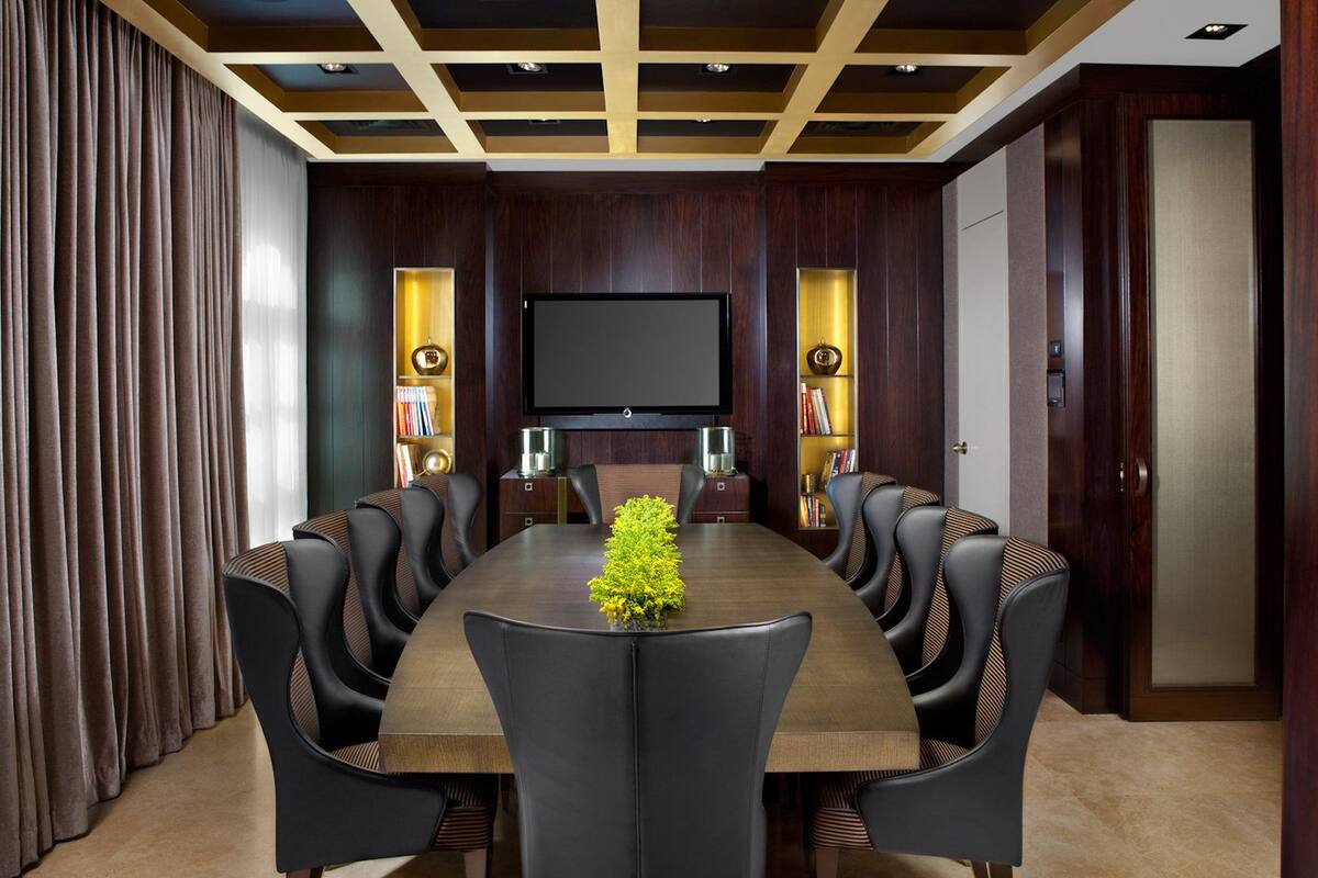 A conference room with a long table, leather chairs, a flat-screen TV, and bookshelves with decorative items.