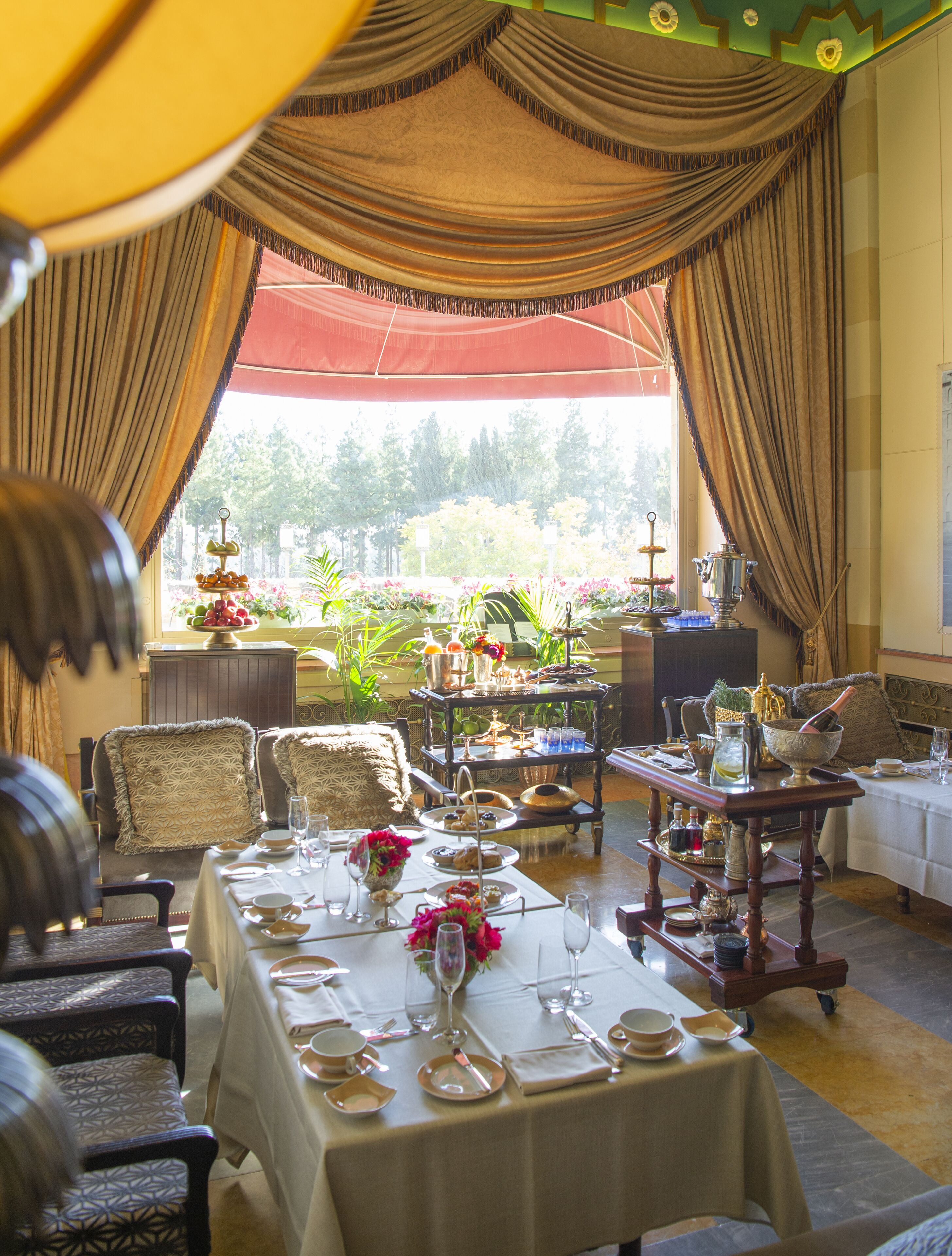 A dining area with a table set for a meal, chairs, a buffet cart, and a view of the outdoors.