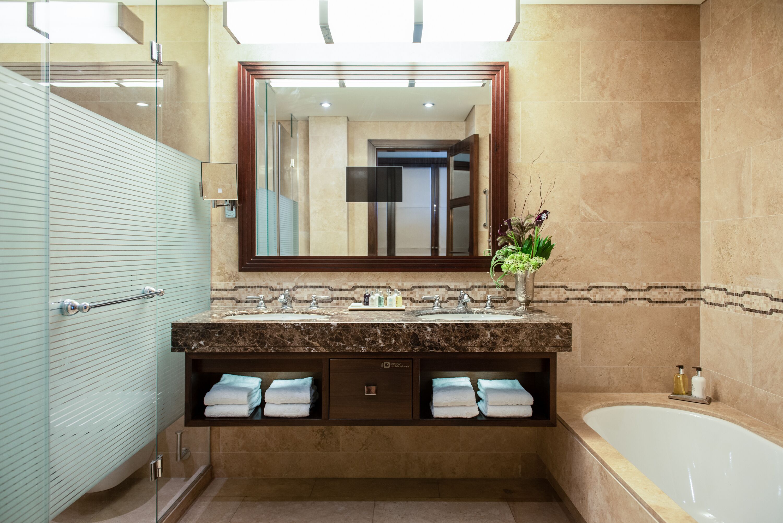 Un baño moderno con cabina de ducha de vidrio, tocador de mármol, espejo grande y bañera.