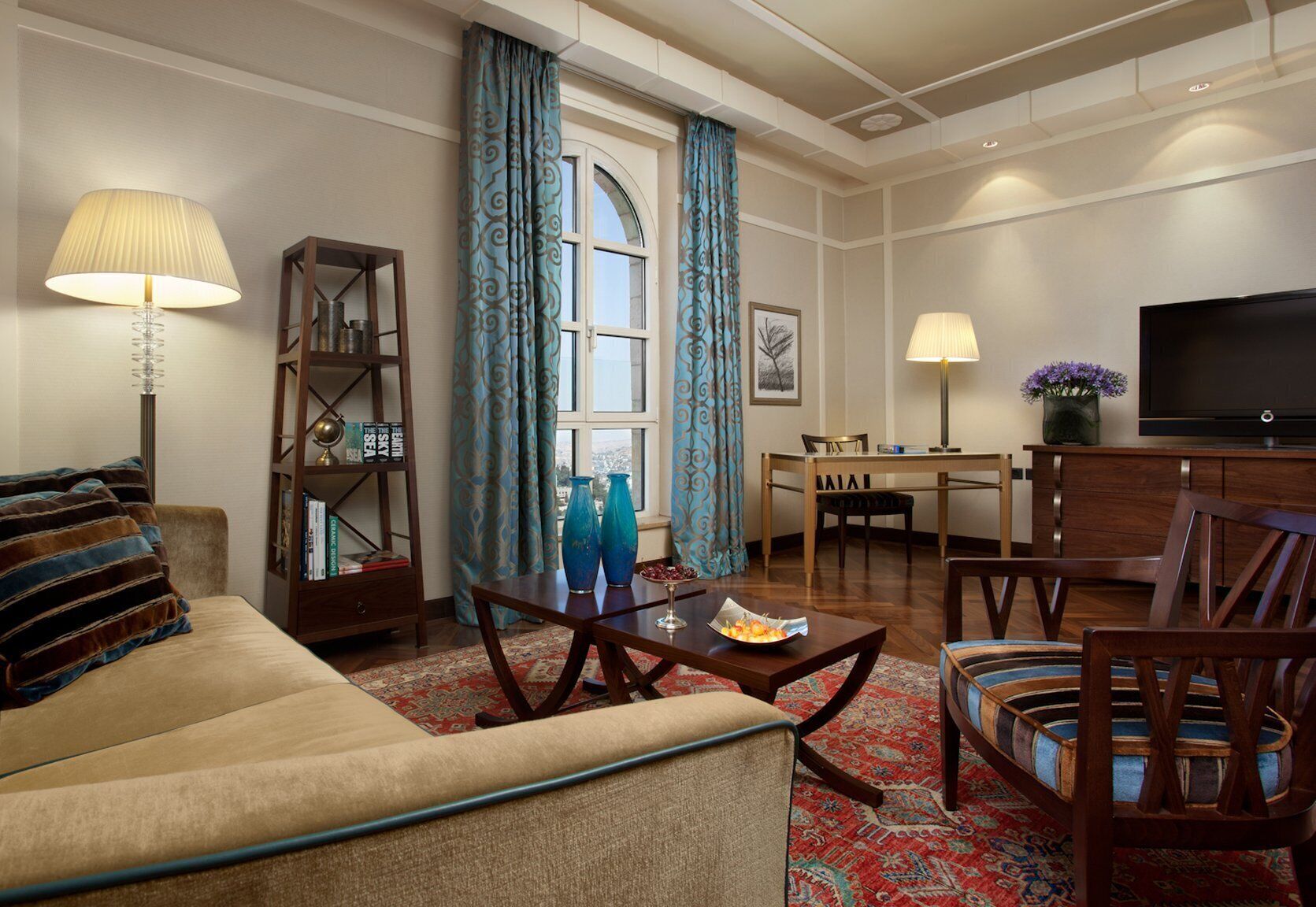 A living room with a sofa, a coffee table, a bookshelf, a dining table with chairs, a television, and patterned curtains.