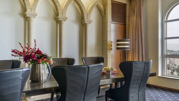 Une salle de conférence avec une longue table, des chaises noires et un vase de fleurs.