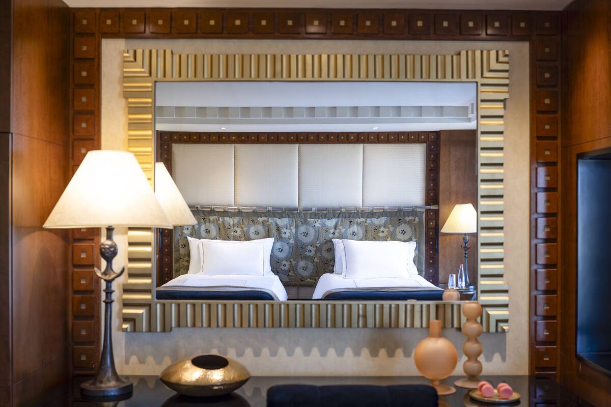 A hotel room with a large bed, two bedside lamps, a decorative mirror, and a small table with a bowl and a vase.