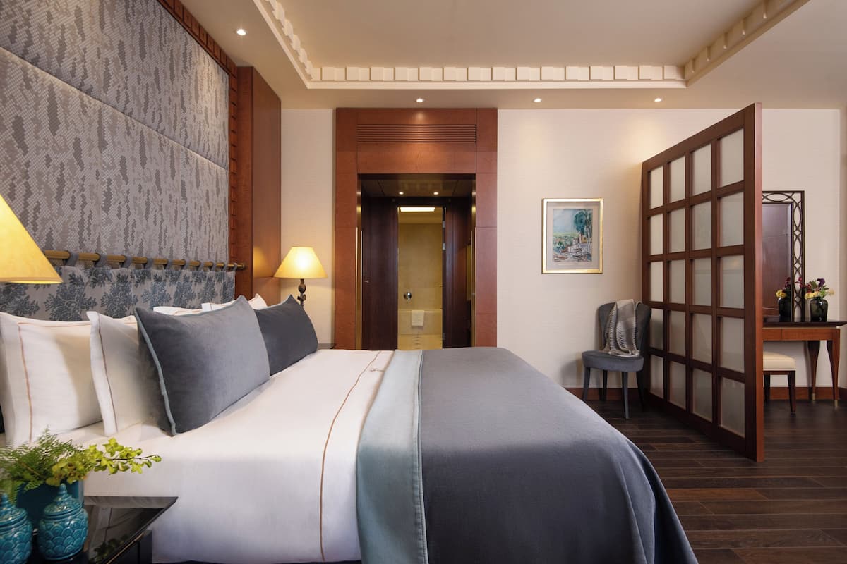 A hotel room with a large bed, a desk with a chair, a wooden partition, and a framed picture on the wall.