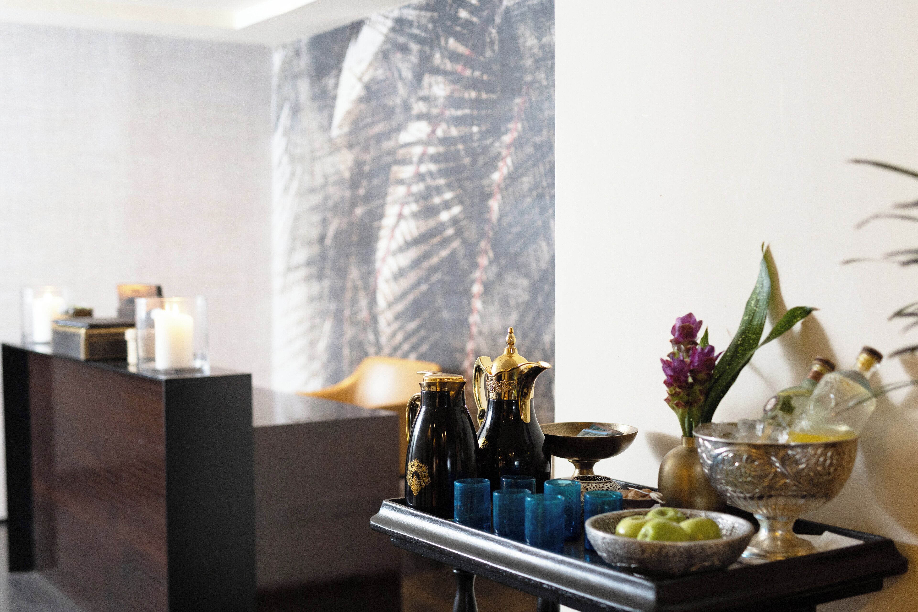 A reception area with a dark wooden reception desk, a large abstract painting on the wall, and a tray with various items including a pitcher, glasses, and a bowl of apples.