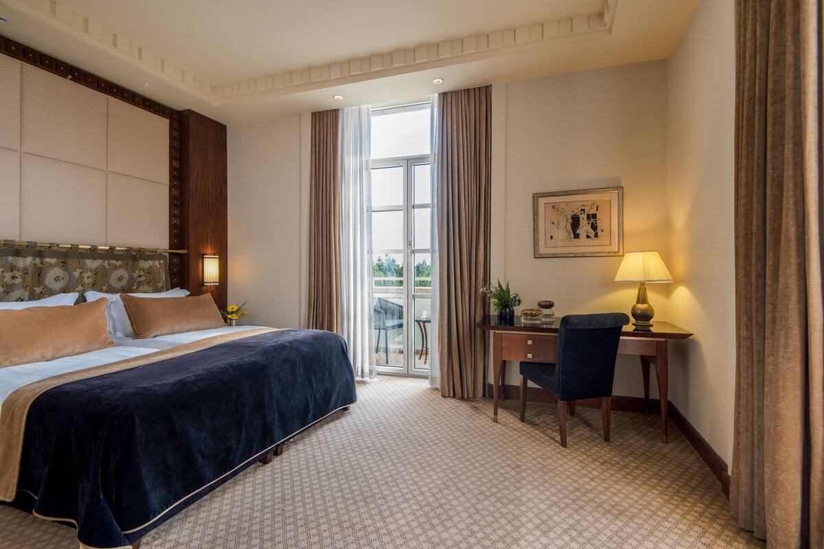A hotel room with a large bed, a desk with a chair, a lamp, and a framed picture on the wall.