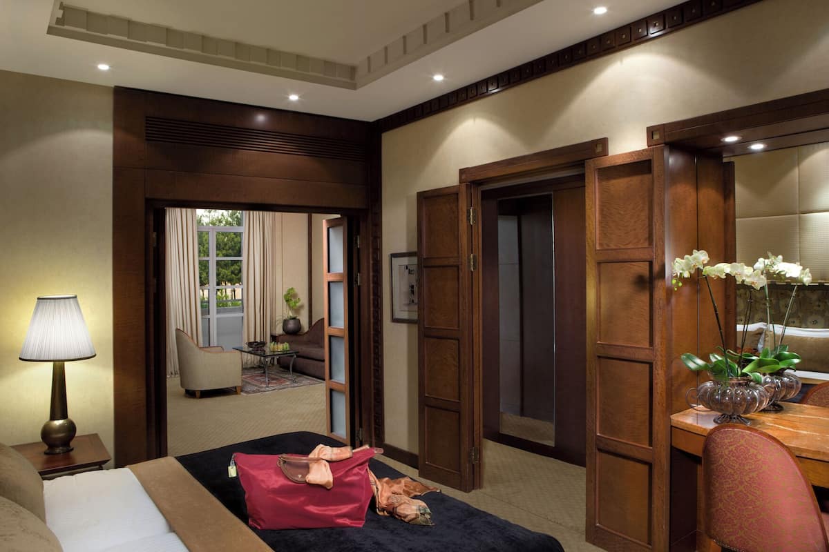 A hotel room with a bed, a desk, a chair, a lamp, and a vase with flowers.