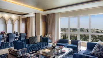 A modern hotel room with a seating area, a dining table, and a view of a cityscape through large windows.