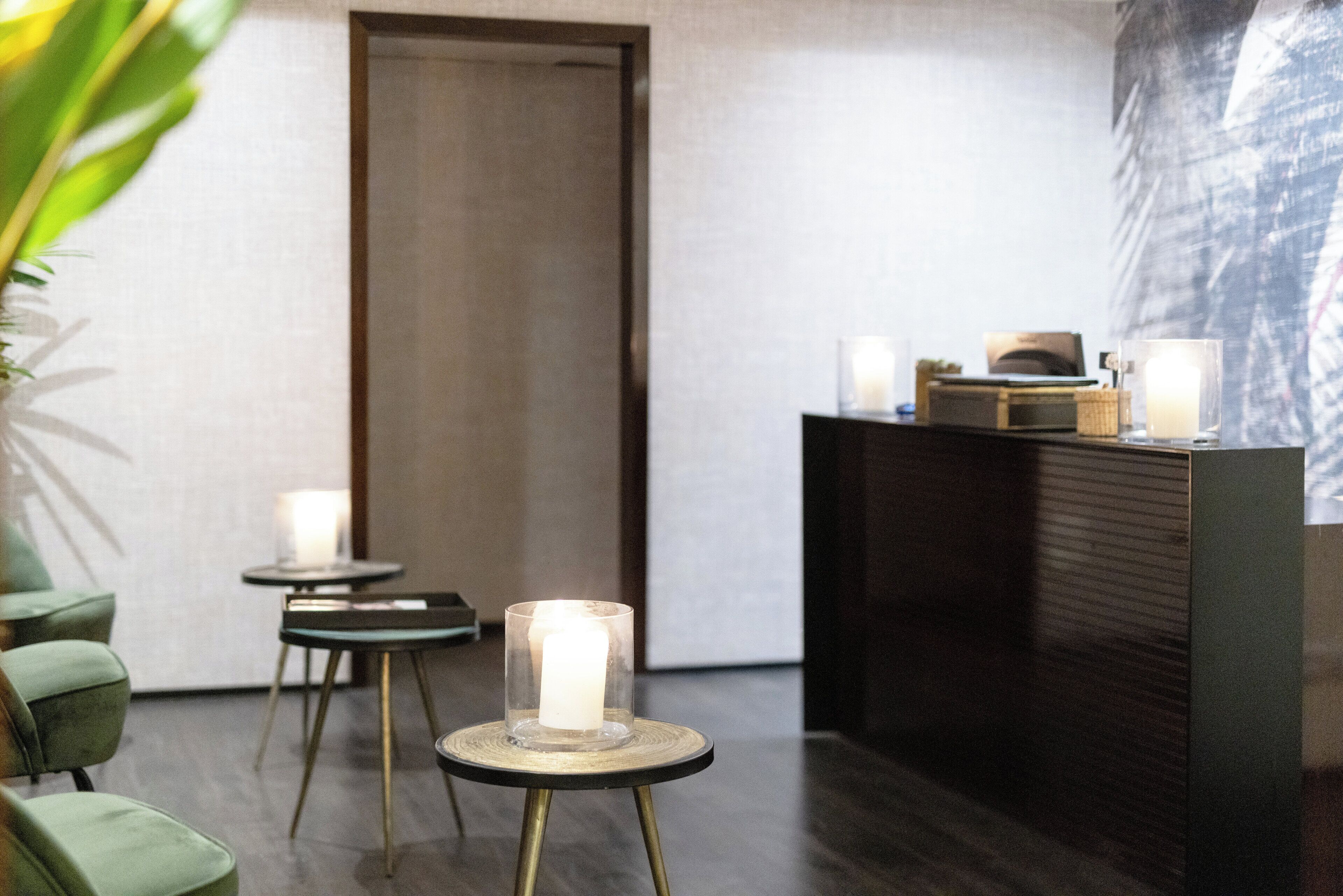 Un interior moderno con un mostrador de recepción, dos mesas redondas con velas y sillas verdes.