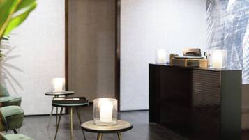 Un interior moderno con un mostrador de recepción, dos mesas redondas con velas y sillas verdes.