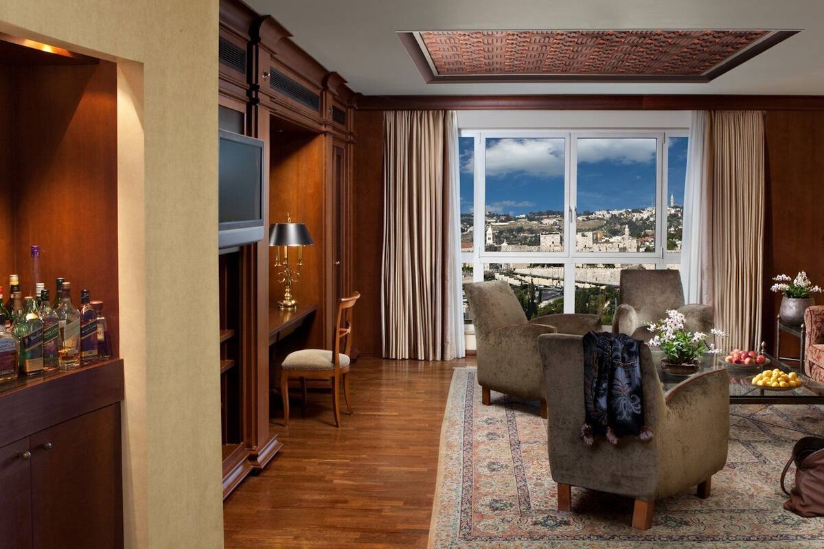 A living room with a large window, a sofa, a chair, a TV, and a cabinet with bottles.