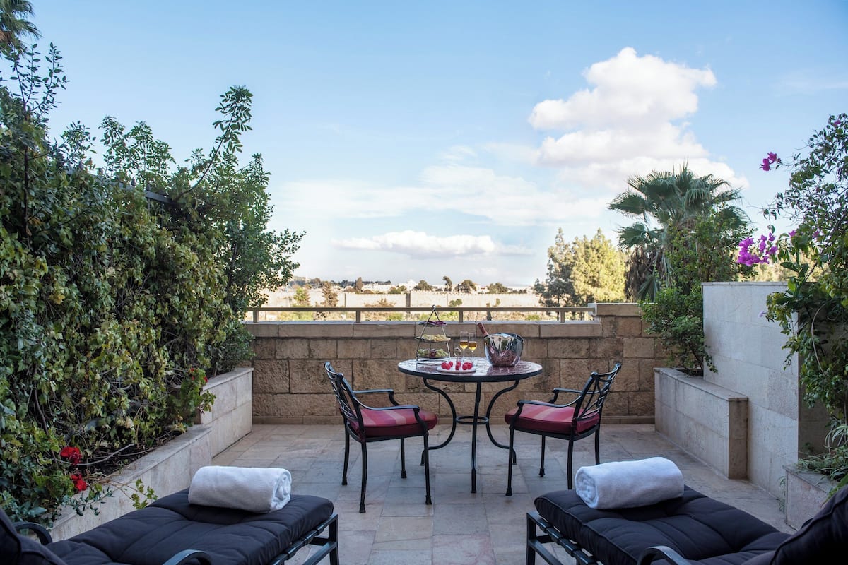 A patio with two lounge chairs, a table with a drink, and a view of the countryside.