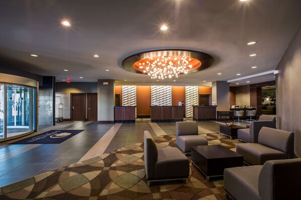 A hotel lobby with a reception desk, seating area, and a large chandelier.