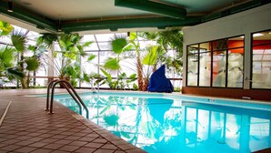 Una piscina interior con agua cristalina y azul, rodeada de grandes ventanales y plantas tropicales.