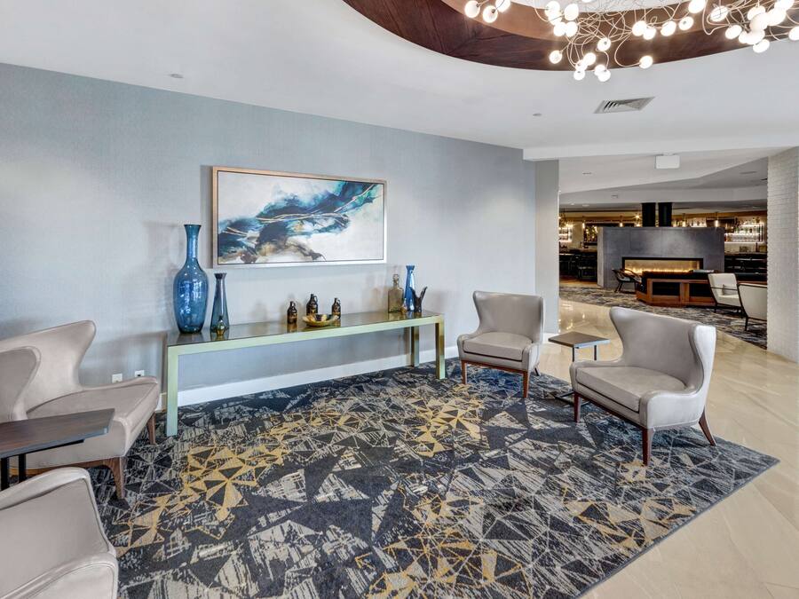 Een moderne lobby met een geometrisch patroon tapijt, een console tafel met decoratieve objecten, en een groot abstract schilderij aan de muur.